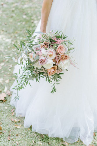 bride holding wedding bouquet of white and peach flowers with greenery