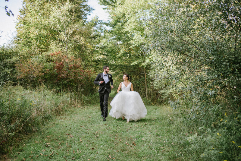groom and bride run through a green pasture