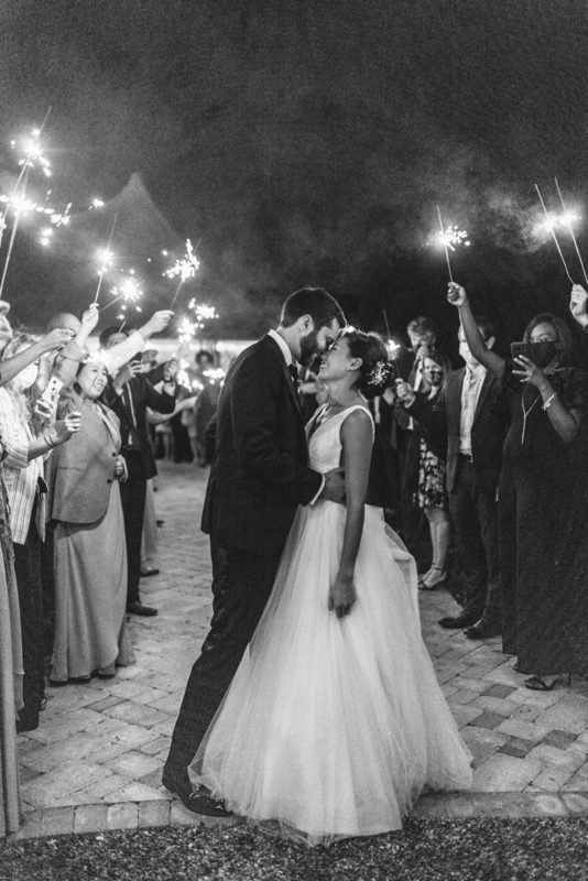bride and groom kiss surrounded by others holding sparklers