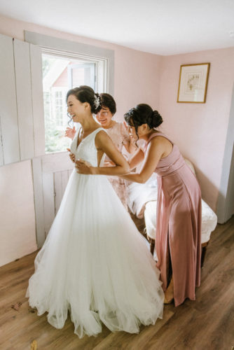 bridesmaids helping bride put her wedding dress on