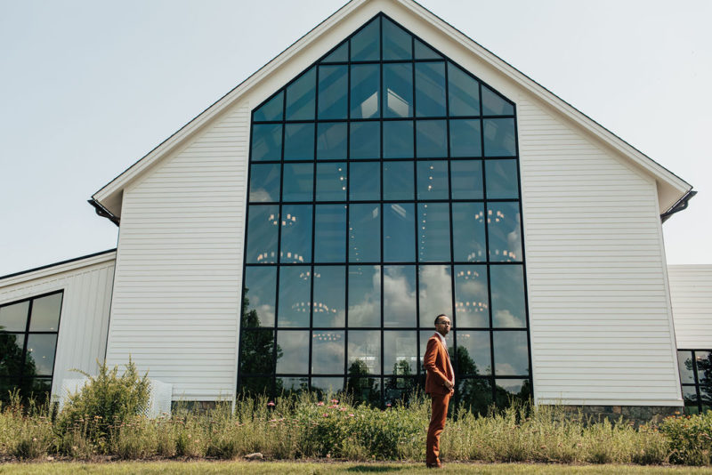 groom waits for bride in front of farmhouse building