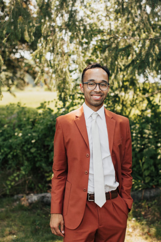 groom poses in rust colored suit