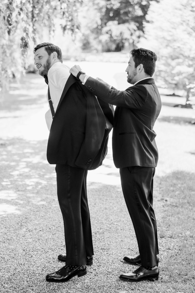 best man helps groom put on suit jacket