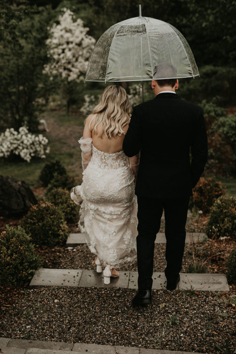 bride and groom walk together with umbrella on a rainy wedding day