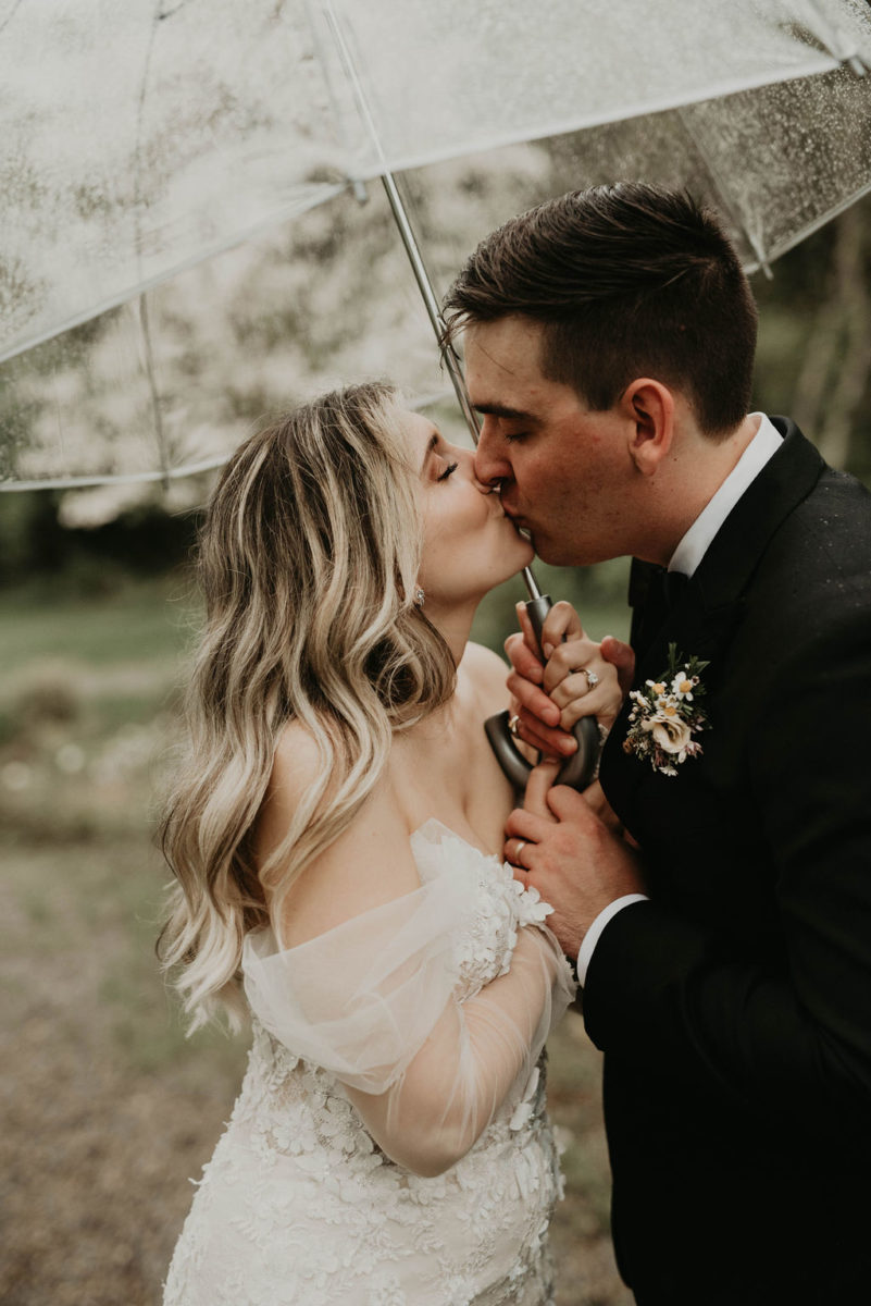 bride and groom kiss under an umbrella on a rainy wedding day