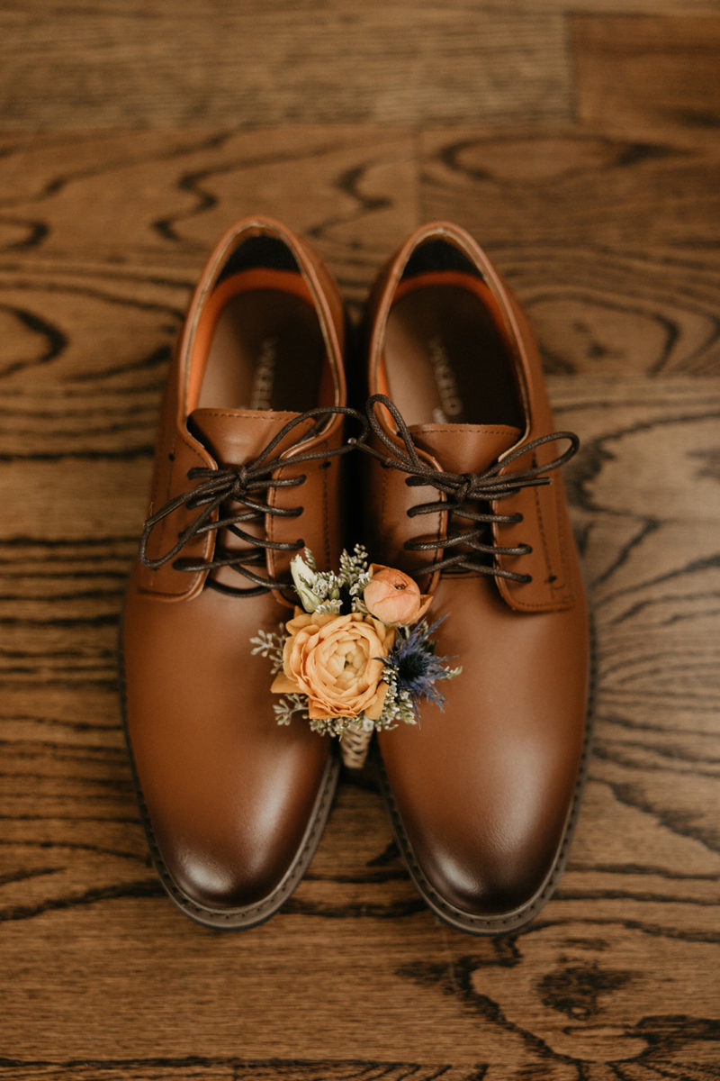 grooms boutonniere sits on top of groom's brown shoes