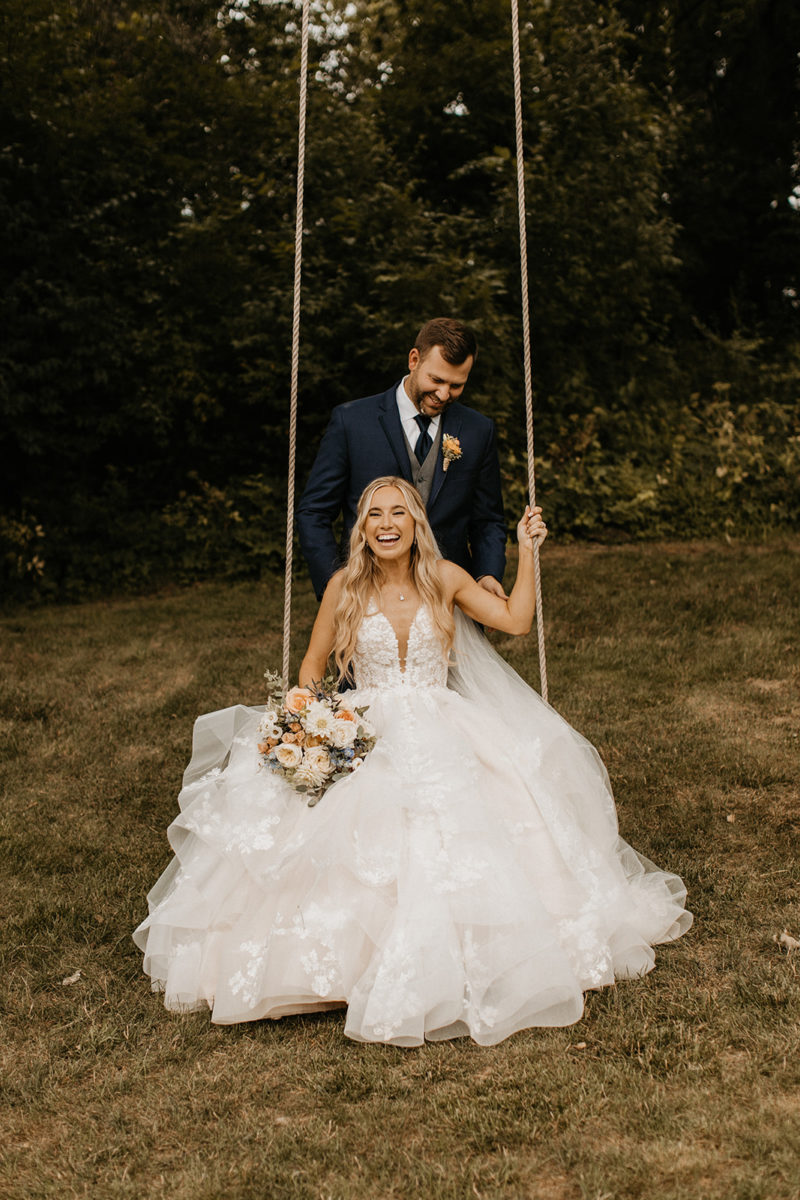 groom pushes bride on a rustic swing
