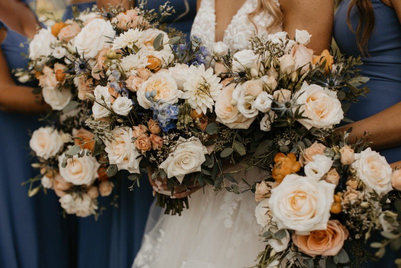 Close up of bride and her bridesmaids holding bouquets of peach and blue flowers