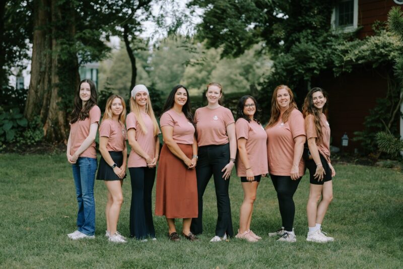 Eight employees of Crossed Keys Estate wearing matching Crossed Keys Designs t-shirts, standing in the grass with lush green summer foliage in the background.