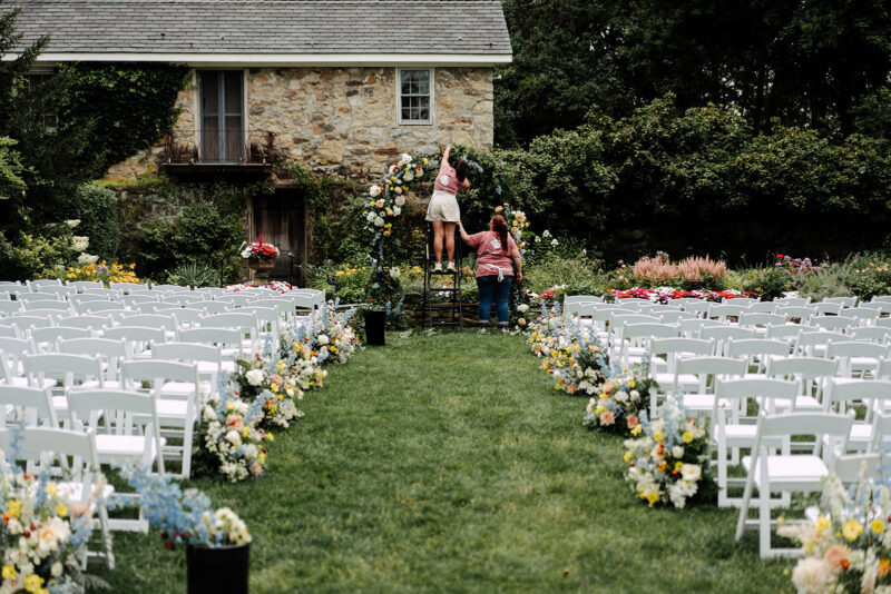 Crossed Keys Design Employees assembling a ceremony arch in the Crossed Keys Estate Garden. Ceremony chair and colorful aisle marker arrangements.