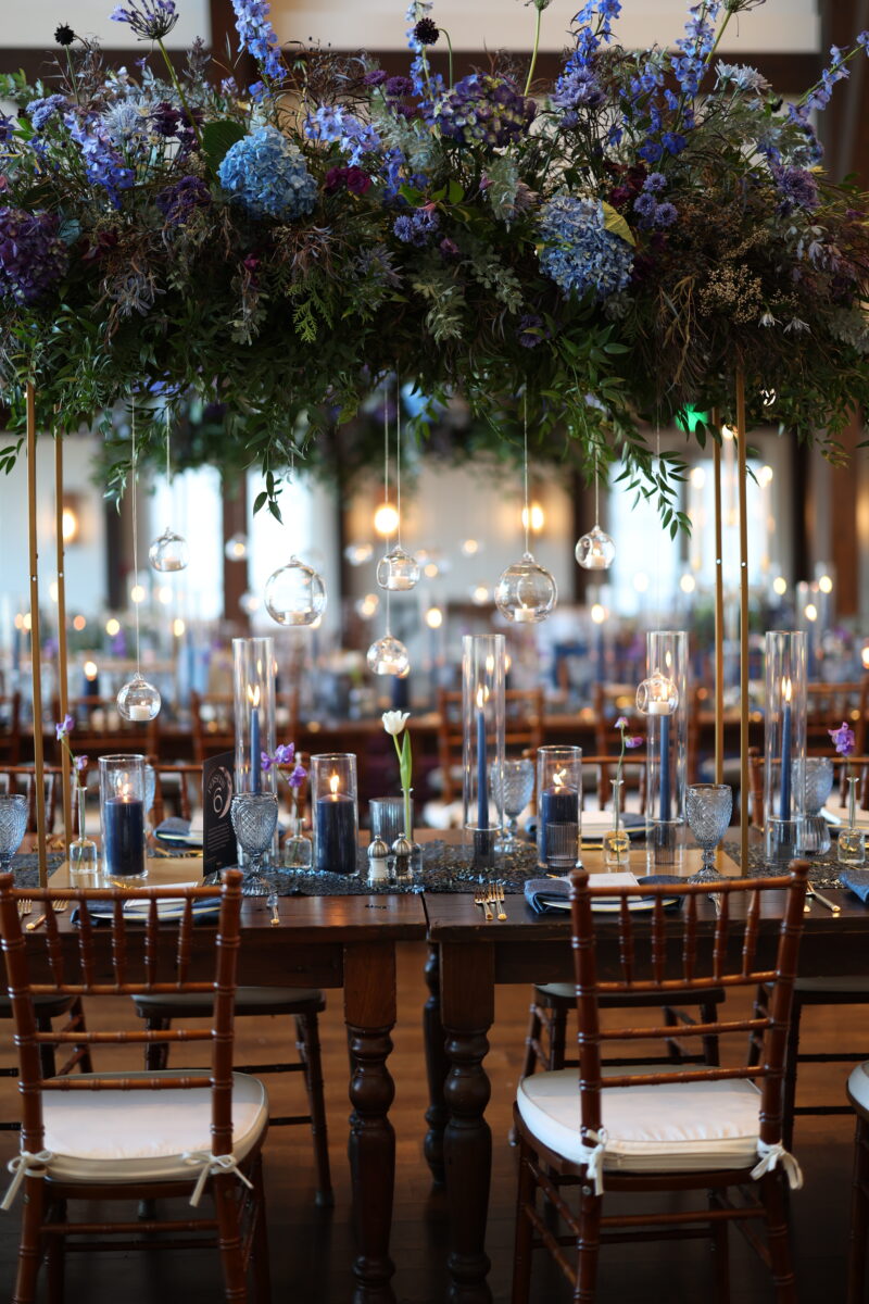 Midnight Blue Wedding, Farmhouse Table, Elevated Hydrangea Arrangement with hanging candle lit bulbs. Blue linens, gold charger, gold silverware