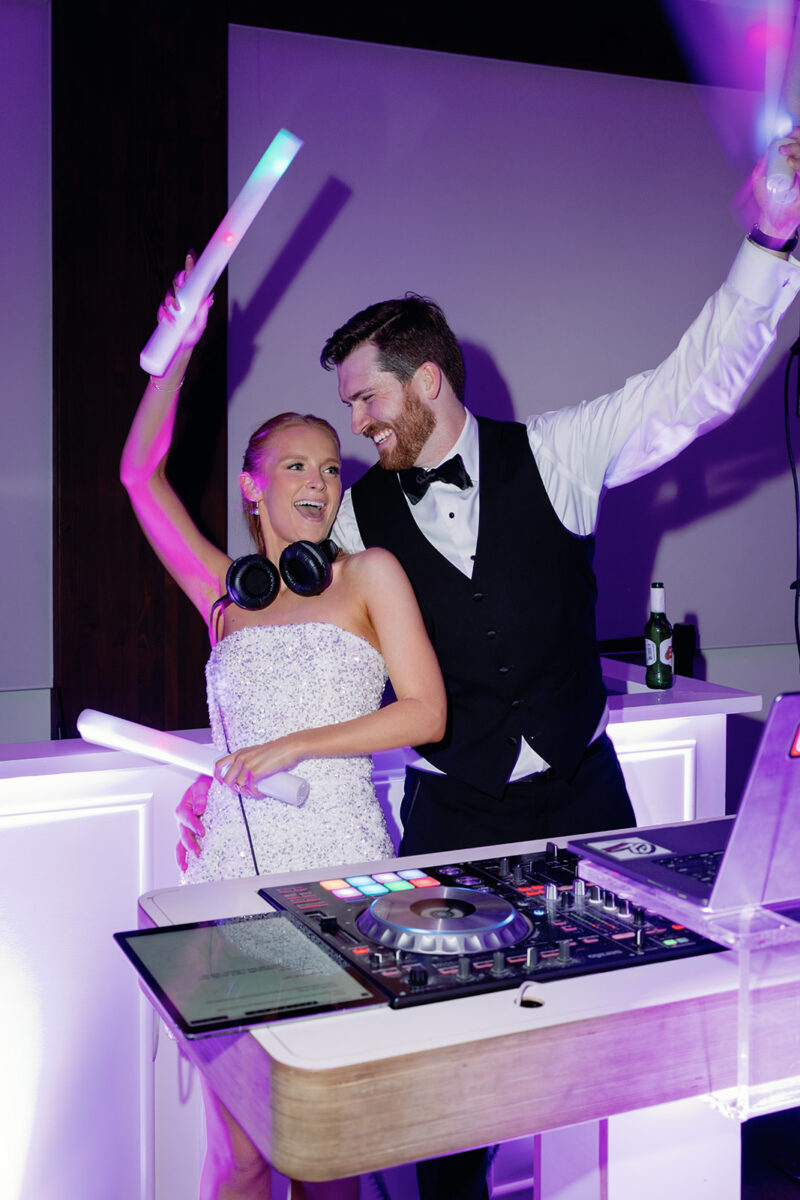 Bride and groom behind DJ booth hyping up guests on dance floor