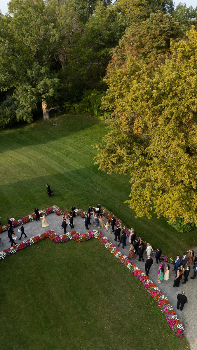 Guests walking from the ceremony to cocktail hour down a flower lined walkway