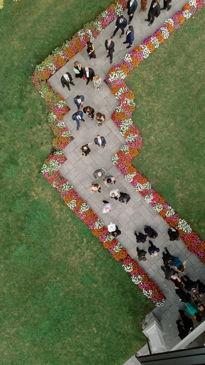 Guests walking from the ceremony to cocktail hour down a flower lined walkway