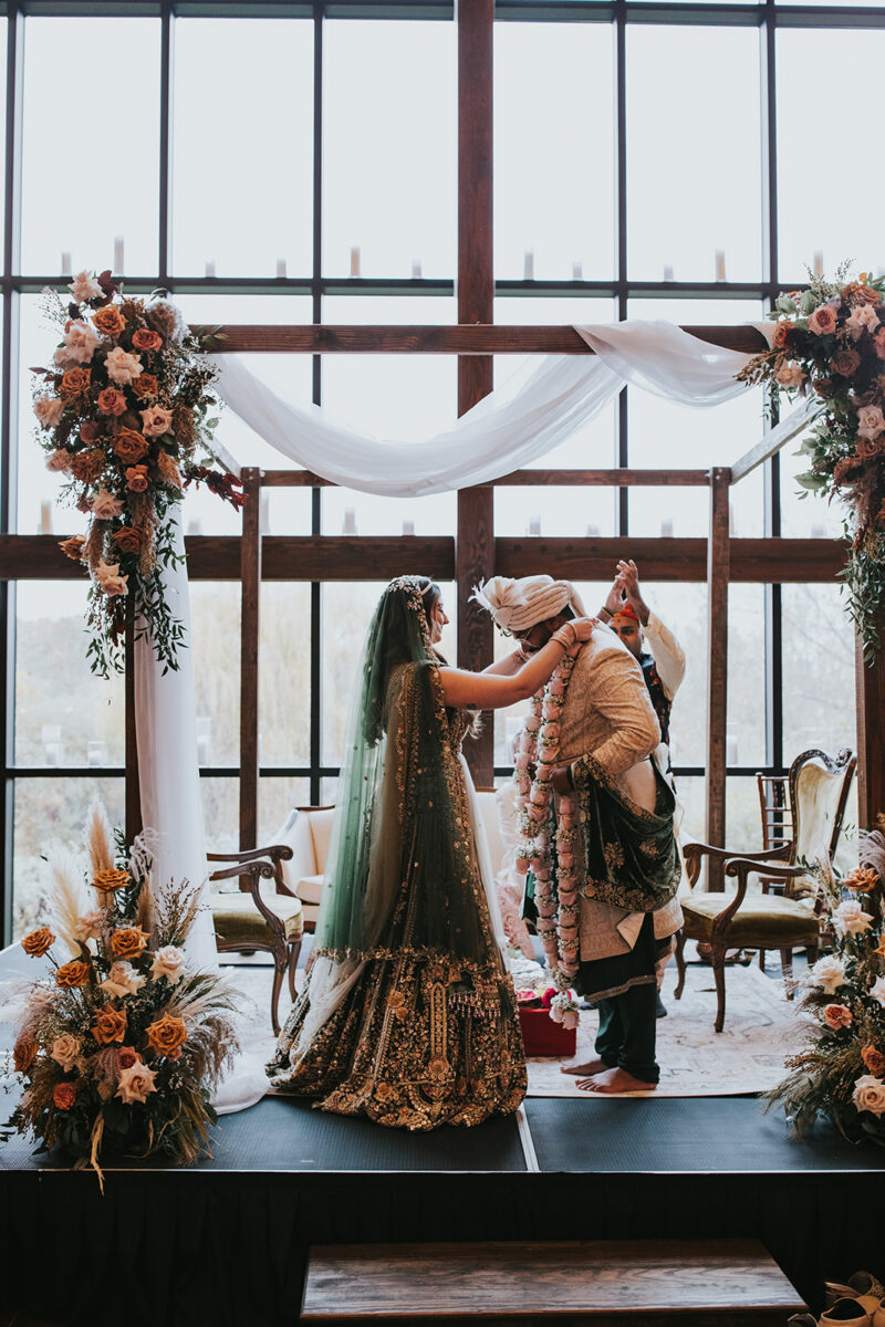 Couple exchanging varmala garlands. Jaimala garland exchange Hindu ceremony mandap setup inside Farmhouse Crossed Keys Estate Indian wedding NJ