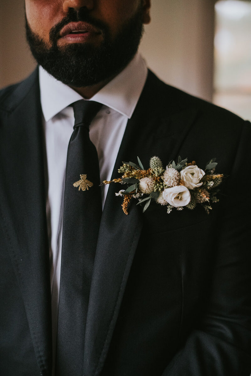 Groom details, pocket boutonniere with mini floral details and boho bee pin on black tie