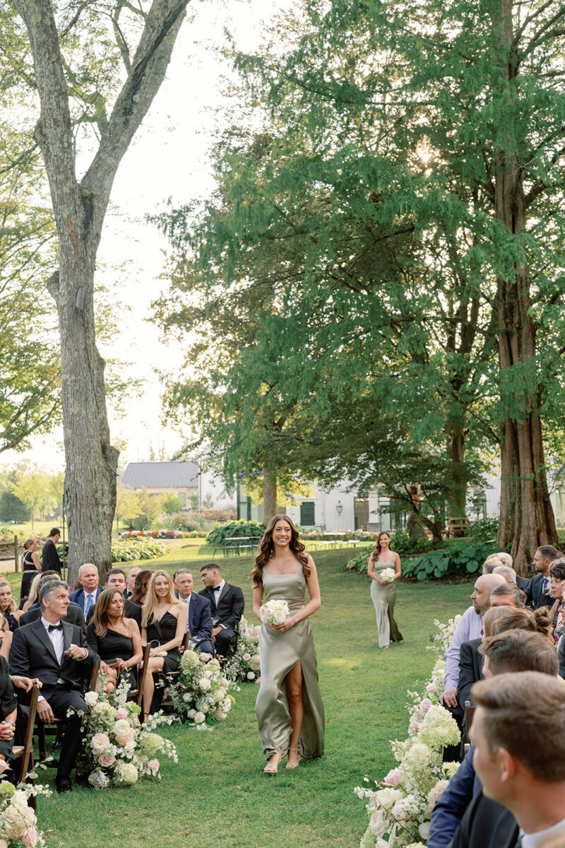 Garden Wedding Ceremony in September. New Jersey Wedding Venue. Bridesmaid with bouquet walking down the aisle.