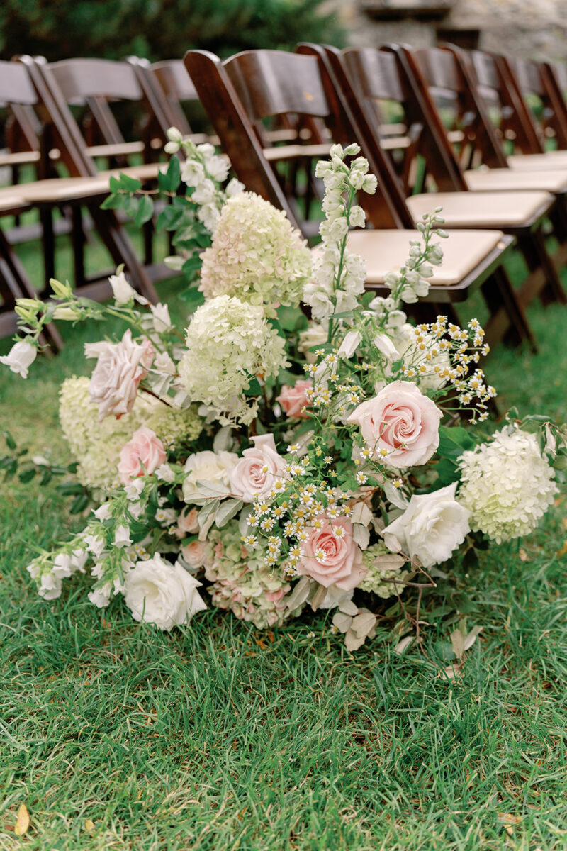 Aisle lined with dark fruitwood chairs and white blush and green floral arrangements
