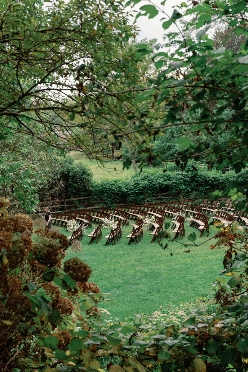 Outdoor ceremony setup under oak trees at Crossed Keys Estate in September. Aisle lined with dark fruitwood chairs and white blush and green floral arrangements